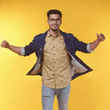 a young man wearing glasses and a denim jacket is standing with his arms outstretched