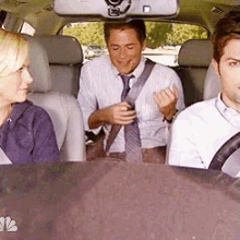 a man and a woman are sitting in the back seat of a car with the nbc logo on the dashboard