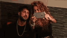 a man and a woman are taking a selfie with their cell phones .