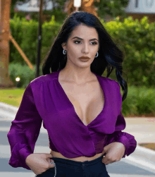 a woman wearing a purple top with a plunging neckline and earrings