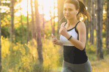 a woman wearing ear buds is running through a forest