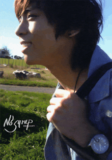 a young man wearing a watch is standing in a field with the website nb syrup in the background