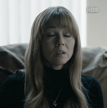 a woman is sitting on a couch with her eyes closed and a hbo logo behind her