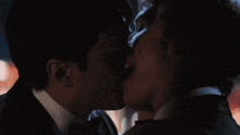 a man in a suit and tie kisses another man in a dark room