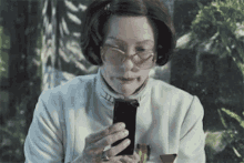 a woman wearing glasses is holding a cell phone in her hand .