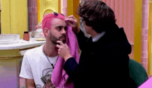 a man with pink hair is getting his hair blow dried by a man with a beard .