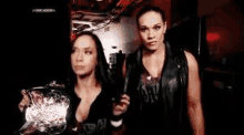 two women are standing next to each other in a dark room holding a wrestling trophy .