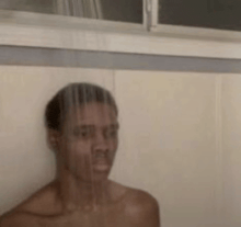 a shirtless man is taking a shower in a bathroom with a window in the background .
