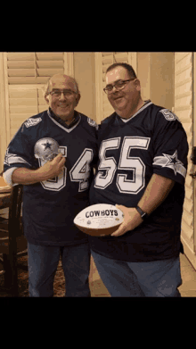 two men wearing cowboys jerseys stand next to each other holding a football