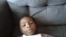 a young boy is laying on a grey couch with his eyes closed