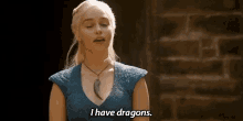 a woman in a blue dress is standing in front of a brick wall and says `` i have dragons . ''