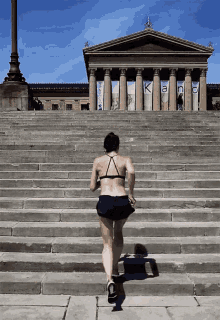 a woman in a bikini is running up a set of stairs in front of a building that has the word kanc on it