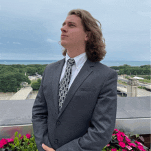 a man in a suit and tie stands on a balcony overlooking the water