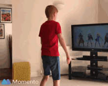 a boy in a red shirt is dancing in front of a television with the word momento on the bottom