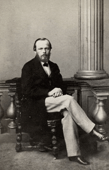 a man sits in a chair with his legs crossed in front of a column