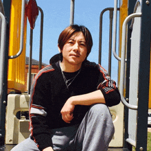 a man in a black and red striped sweater sits on a playground