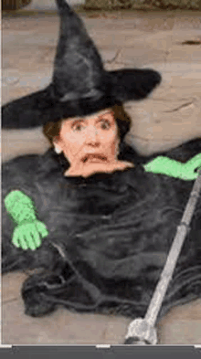 a woman in a witch costume is laying on the ground holding a cane .