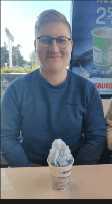 a man in a blue sweater is sitting at a table with a cup of ice cream