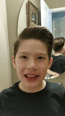 a young boy smiles in front of a mirror with a framed picture on the wall behind him