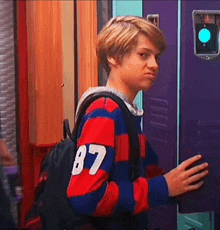 a young boy wearing a striped sweater and a backpack is standing in front of a vending machine .