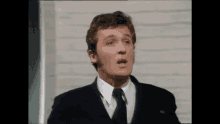 a man in a suit and tie is making a funny face while standing in front of a brick wall .