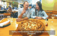 a man and a woman are sitting at a table with a pizza and a caption that says shooting a moose