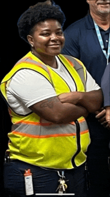 a woman wearing a yellow vest and a white shirt is smiling with her arms crossed