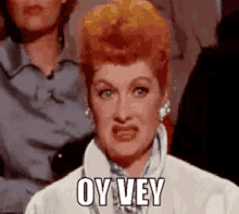 a woman with red hair is sitting in a crowd and making a funny face while saying oy vey .