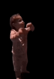 a baby is standing in the dark with his arms outstretched