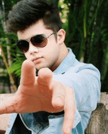 a young man wearing sunglasses and a blue jacket points his finger