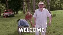 a man in a hat is walking through a grassy field with the words welcome written on the ground .