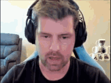 a man with a beard is wearing headphones while sitting in front of a computer screen .