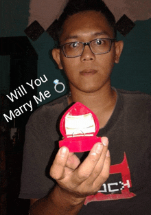 a man wearing glasses is holding a box with a ring in it and the words " will you marry me " above him