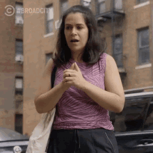 a woman in a zebra print tank top is standing in front of a brick building with #broadcity written on the bottom right