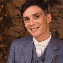 a man in a blue suit and white collared shirt smiles for the camera