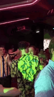 a group of people are dancing in a dark room and one of them is wearing a yellow shirt with bananas on it