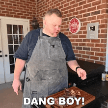 a man in an apron holds a piece of meat in front of a brick wall that says dang boy