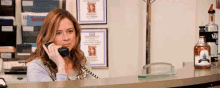 a woman is talking on a phone while sitting at a counter with a bottle of vodka in the background