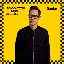 a man wearing glasses stands in front of a yellow and black checkered background that says danke on it