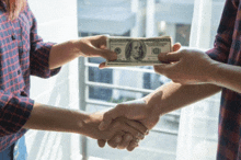 two people shaking hands while one holds a 100 dollar bill