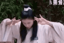 a woman in a kimono is covering her ears with her hands while standing in front of a bamboo forest .