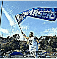 a man in a diego chargers jersey holds up a blue flag