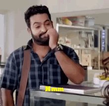 a man with a beard wearing a plaid shirt and a watch is standing in front of a counter .