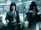 a man in a blue jacket is standing next to another man in a black hat