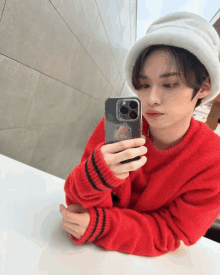 a person wearing a red sweater and a white hat is taking a selfie