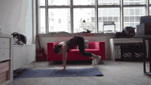 a woman is doing push ups on a yoga mat in front of a red couch and a sign that says " no smoking "