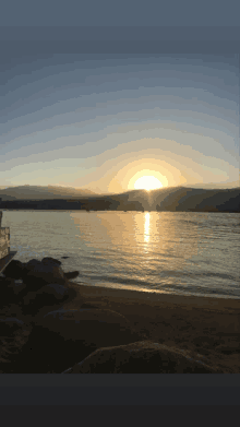 the sun is setting over a lake with mountains in the background