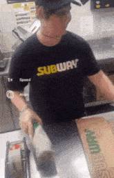 a man wearing a black shirt that says subway is standing at a counter