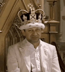 a man is sitting on a throne wearing a crown and a white suit .