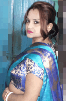 a woman in a blue saree stands in front of a door